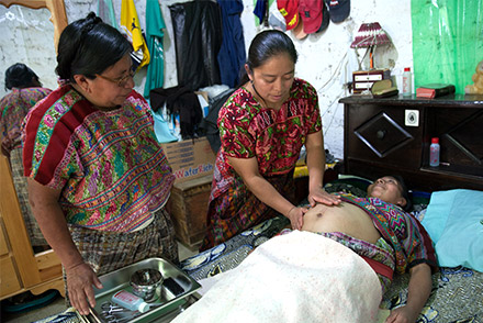 Gloria works with a pregnant woman in her clinic while a colleague looks on.