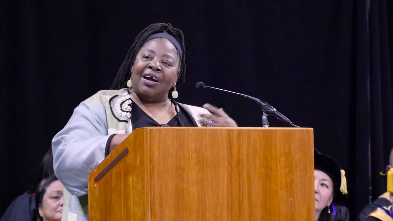 Loretta Ross standing at a speakers podium and speaking into a microphone