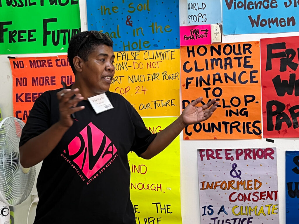 Kado from DIVA for Equality stands in front of a wall of colorful hand drawn climate justice posters.