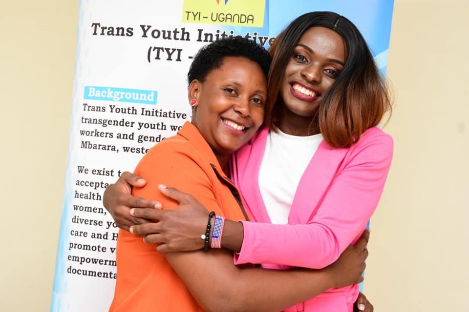 Two Ugandan trans rights activists smile and embrace one another.