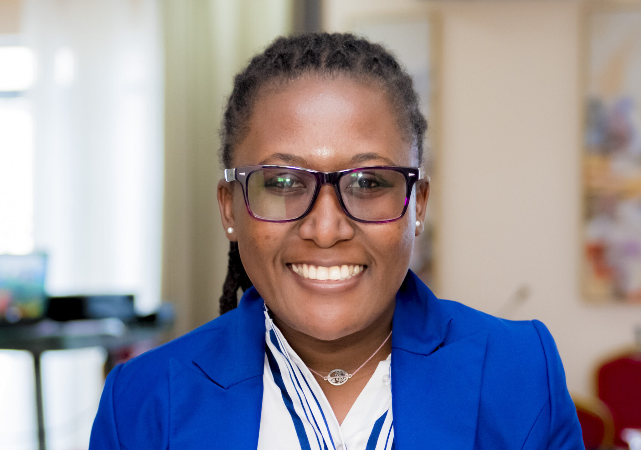 Joanita Babirye smiles for the camera while wearing glasses and a blue jacket.