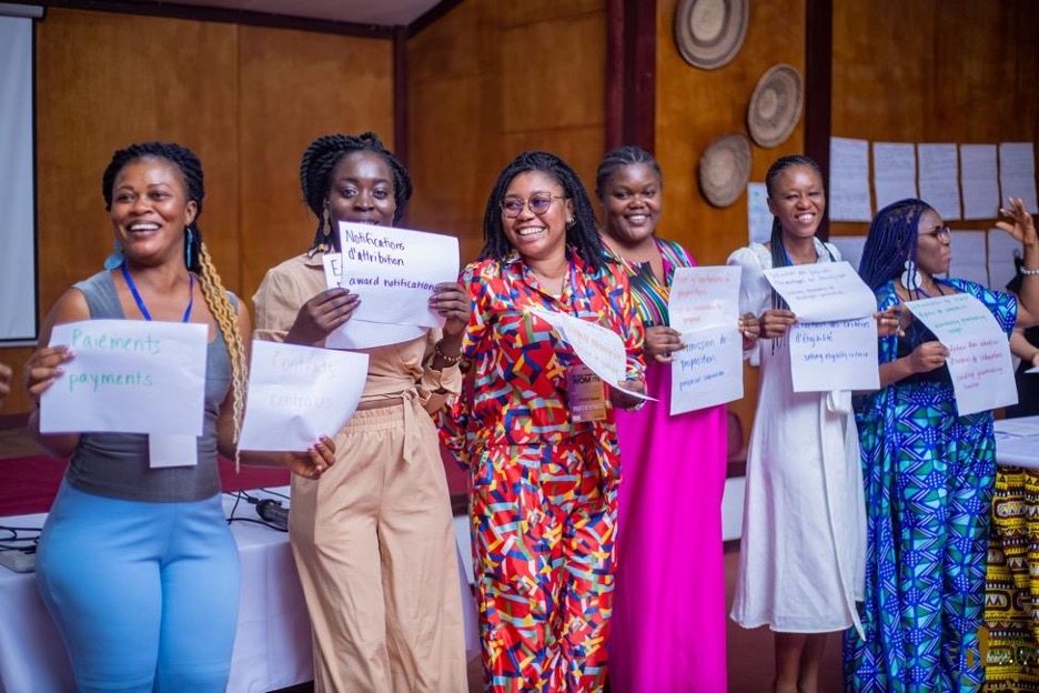 Six of the eight Movement Committee members are smiling while they stand in a line holding signs, each one describing a step in the participatory grantmaking process. This activity asked members to share reflections about each step to inform their recommendations for process improvement.